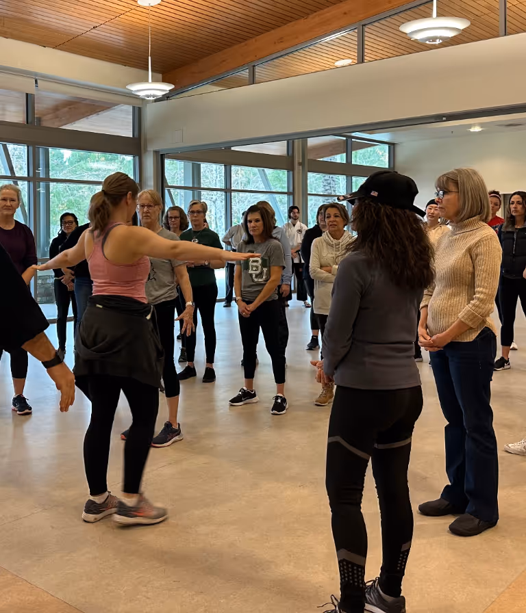 A group of women's self defense class students gather around to observe a tactical demo by a volunteer.