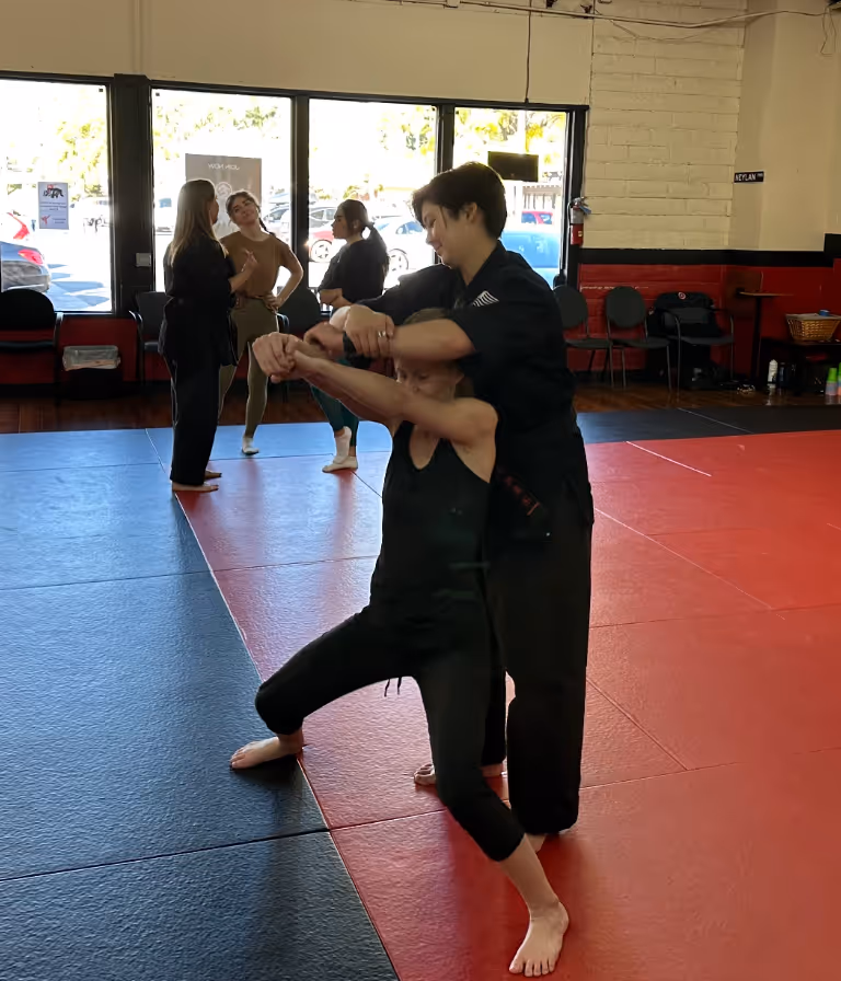 Two women practicing grab defense tactics during women's self defense class.