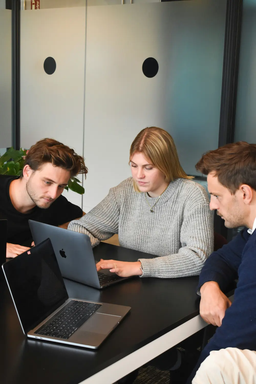 Team aus 3 Leuten sitzt am Tisch und gucken auf einen Laptop