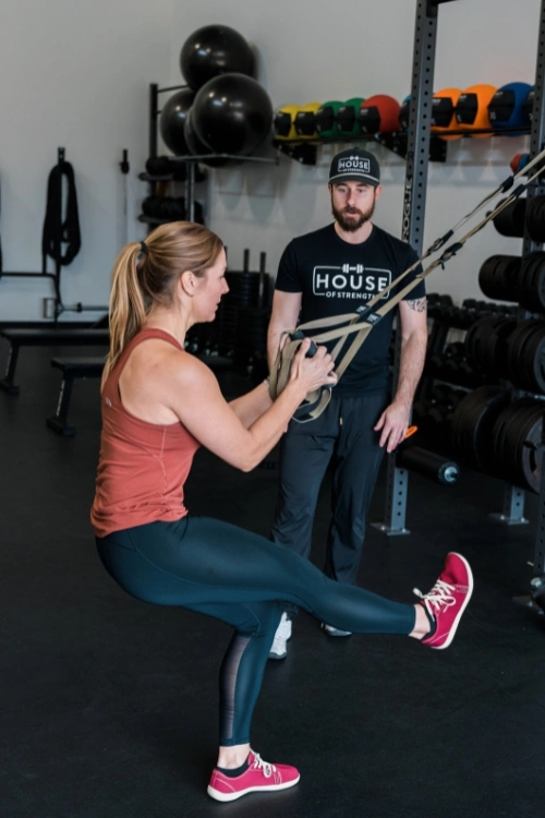 Woman completing squat training with a coach at House of Strength