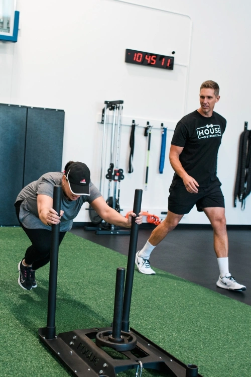 Woman completing a sled push with a House of Strength coach
