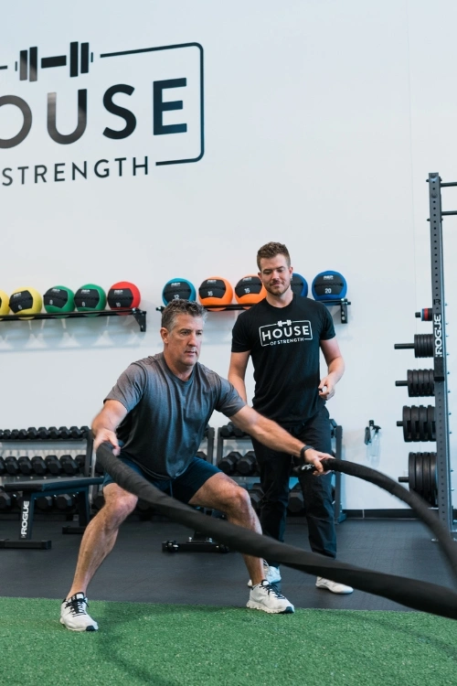Adult client completing battle rope training with a House of Strength coach