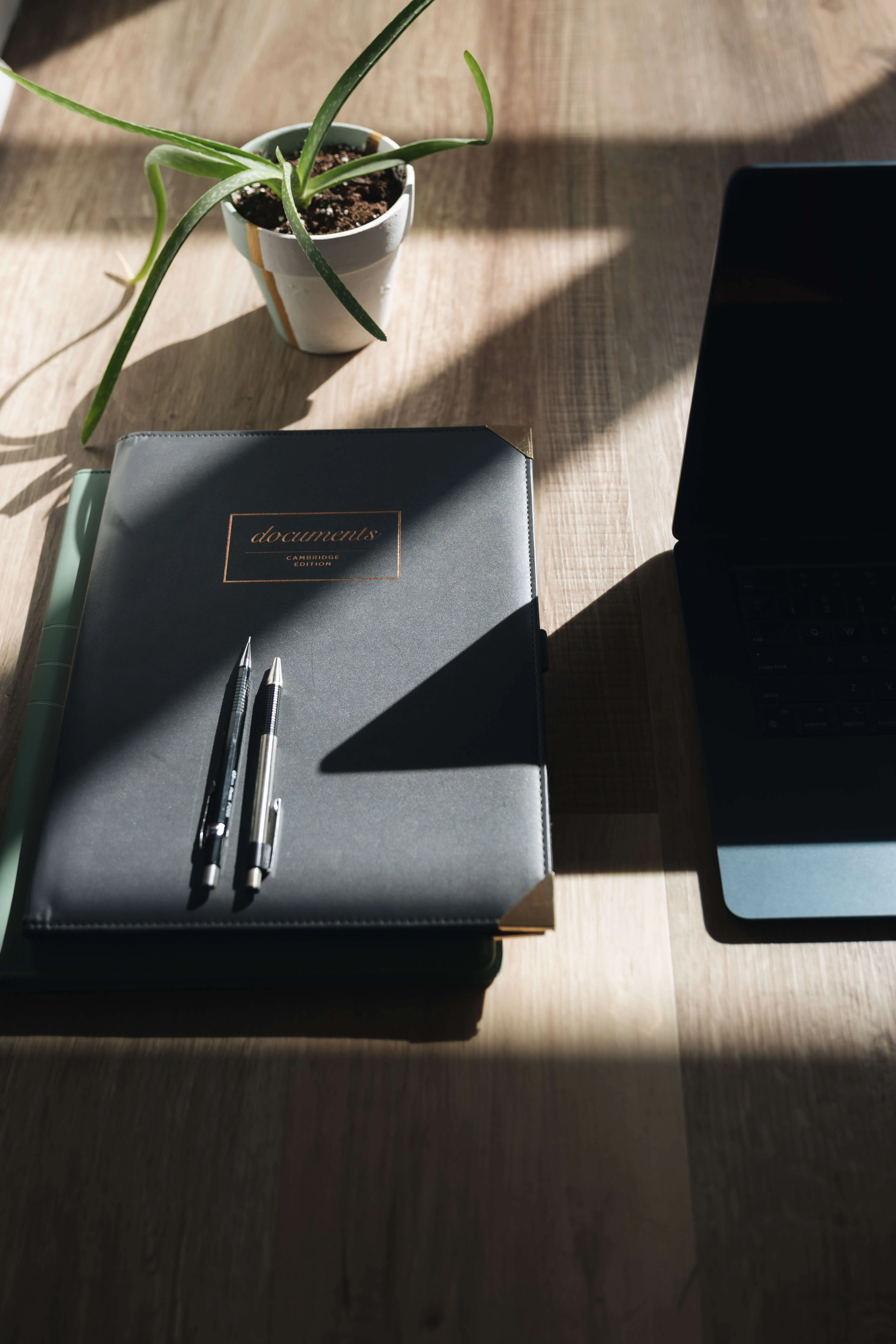 Black notebook on a wooden table next to an open laptop