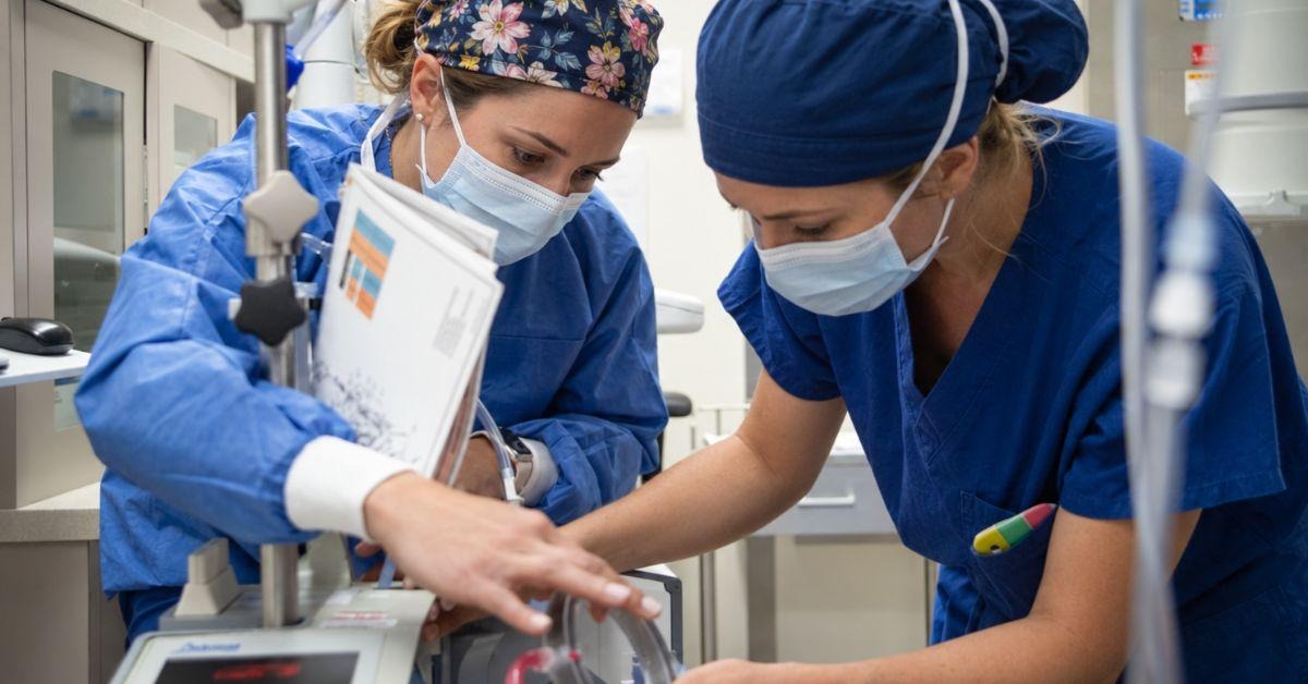 Two theatre staff in scrubs preparing anaesthetic equipment before a surgical list