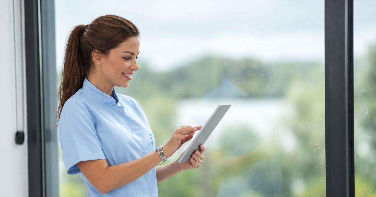 Nurse in a blue uniform checking patient notes on a tablet