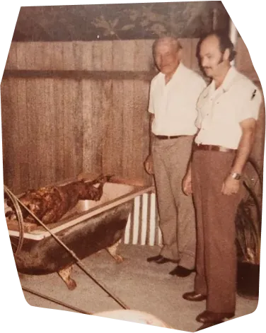 an old photo of two men roasting a pig