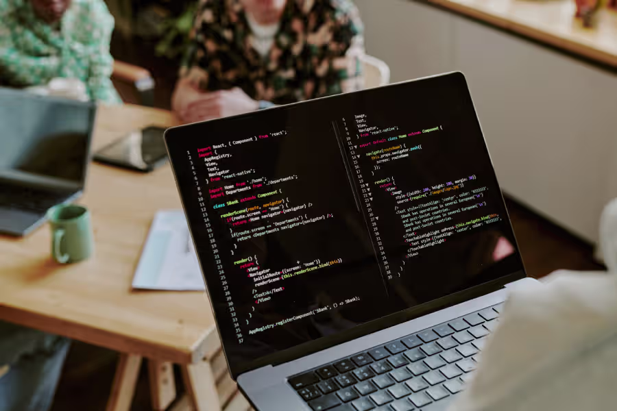 Individual seated at a table with a laptop showing code related to SuiteScript 2.1 and its ES6 features.