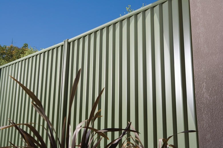 Tall light green Colorbond steel fence with vertical corrugated panels