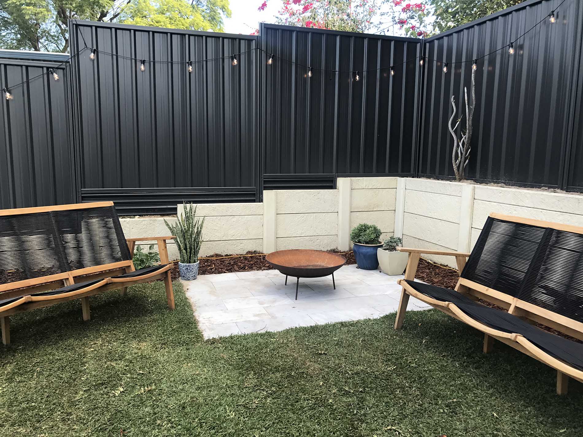 Modern backyard with black Colorbond steel fencing, string lights, and a cozy patio area