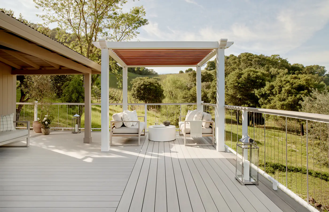 TimberTech composite deck with light gray boards, cable railings, and a modern white pergola with outdoor seating overlooking a lush landscape