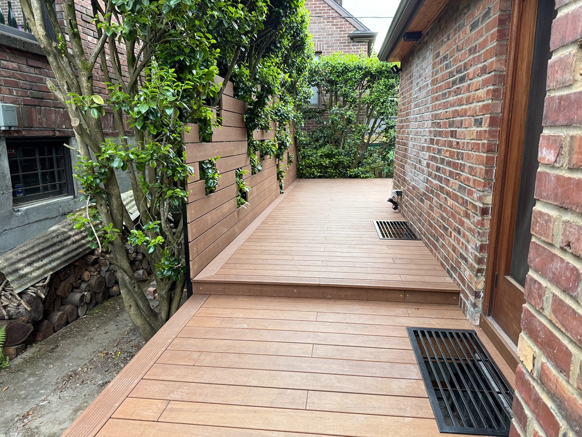 Side view of new composite deck beside a brick home in Bellevue; step-down landing and modern privacy screen with plant openings