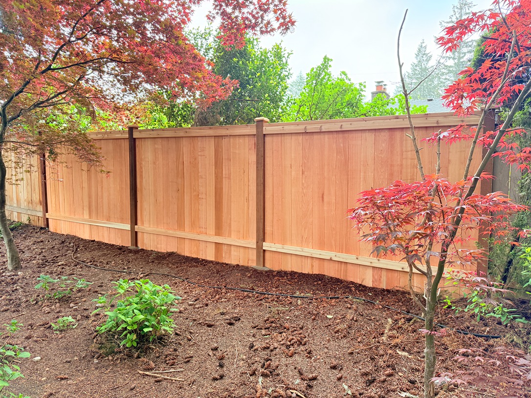 Back view of an estate fence with vertical cedar boards, horizontal rails, and exposed posts