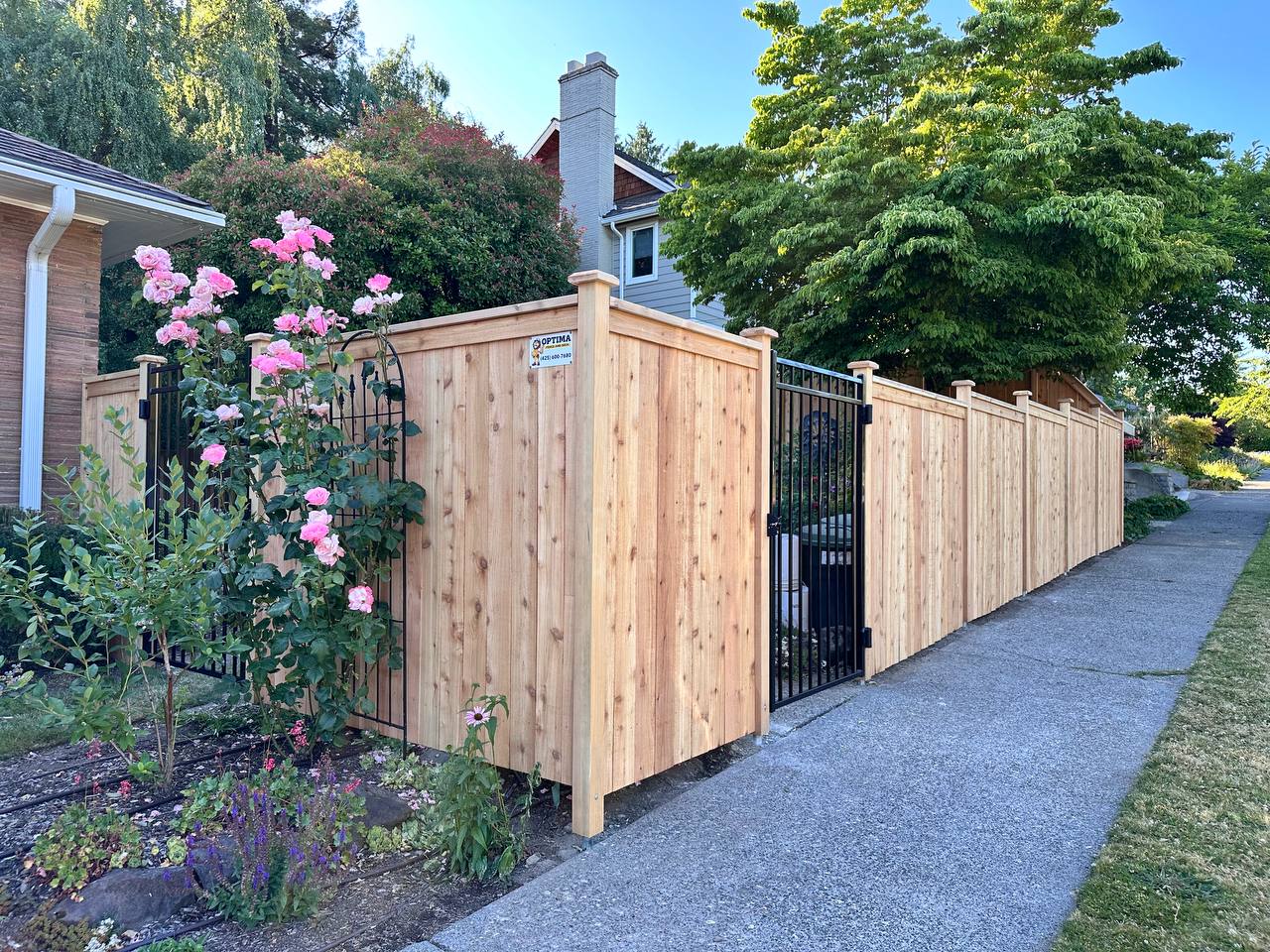 Modified full panel cedar fence with a black metal gate along a sidewalk
