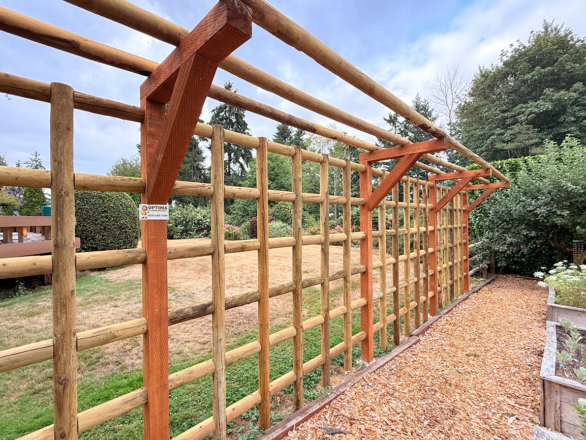 Custom log-style cedar fence with open lattice grid and overhead beam structure installed in a residential garden