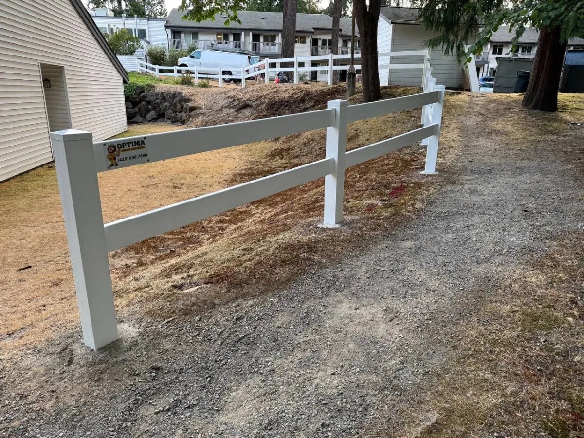 Close-up of a vinyl fence post base securely set in concrete on gravel ground during a professional ranch rail fence installation