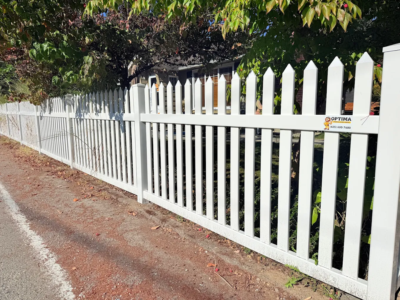 White vinyl picket fence bordering a front yard garden with lush green landscaping and flowering plants at a residential Bellevue home