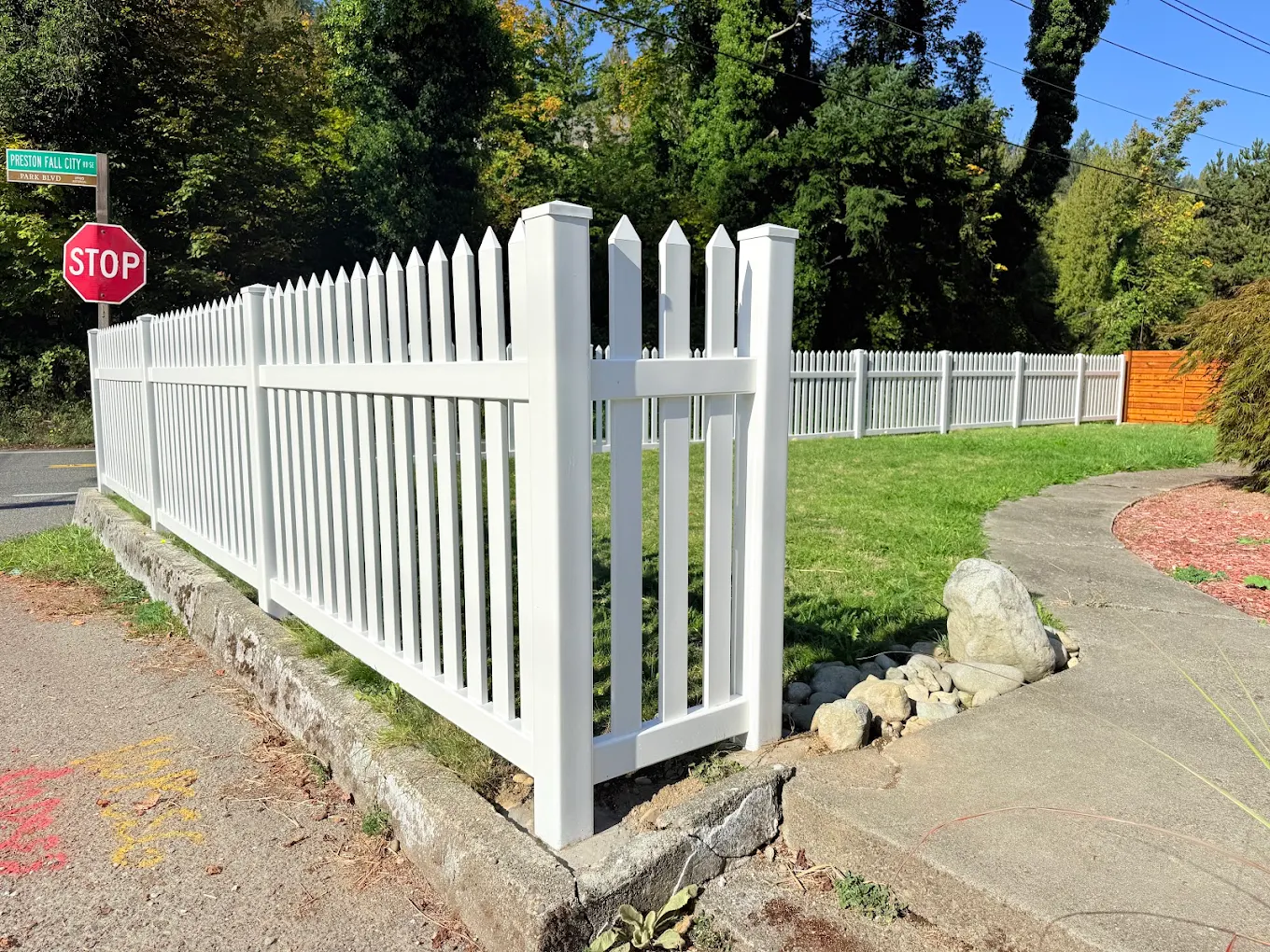 White vinyl picket fence installed at a tan craftsman-style home with tall Pacific Northwest evergreen trees in the background