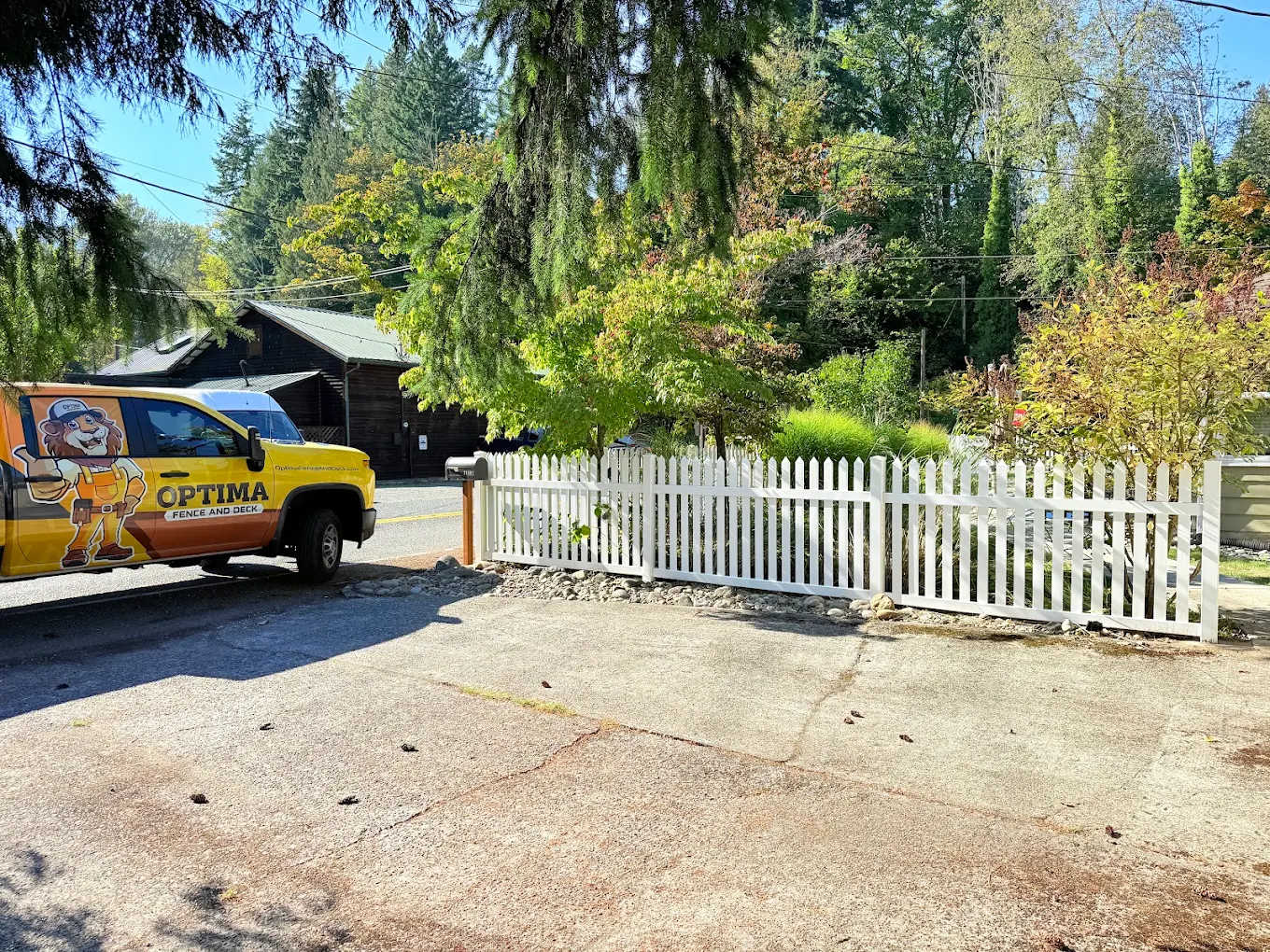 White vinyl picket fence at a residential property with an Optima Fence and Deck branded yellow work truck parked nearby