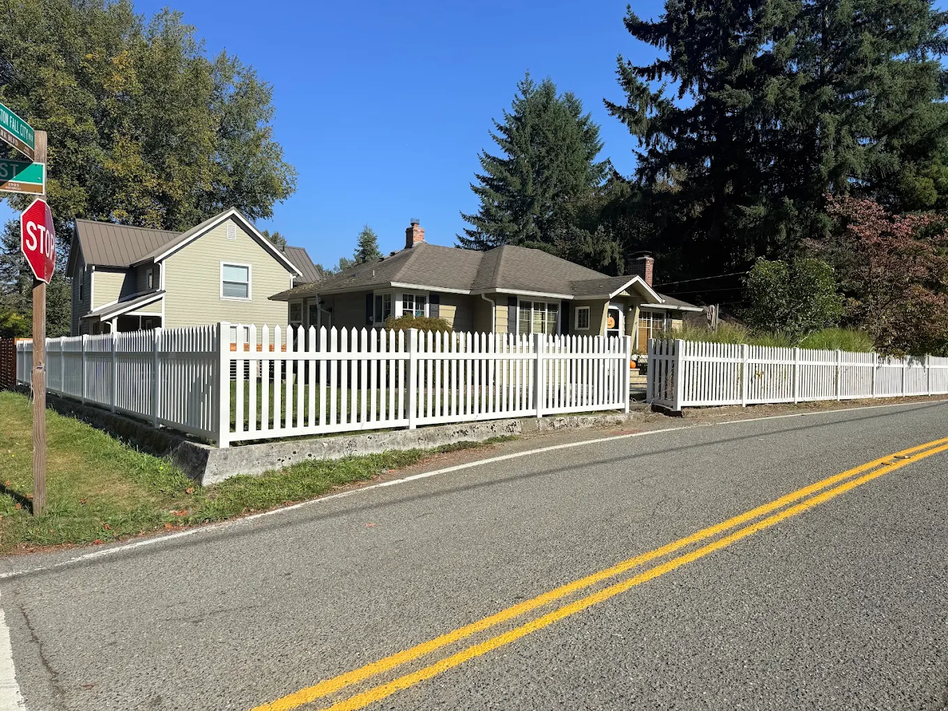 White vinyl picket fence running alongside a residential road with yellow center lines and a sidewalk in a Bellevue neighborhood