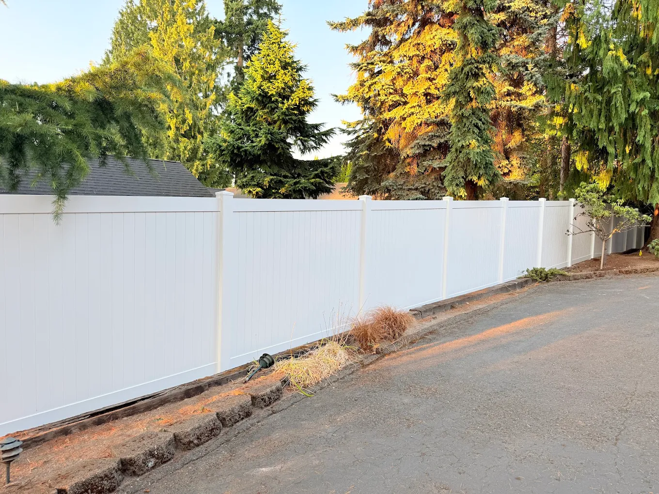 White vinyl privacy fence along a hillside property with fall-colored trees and residential homes visible in the Bellevue area