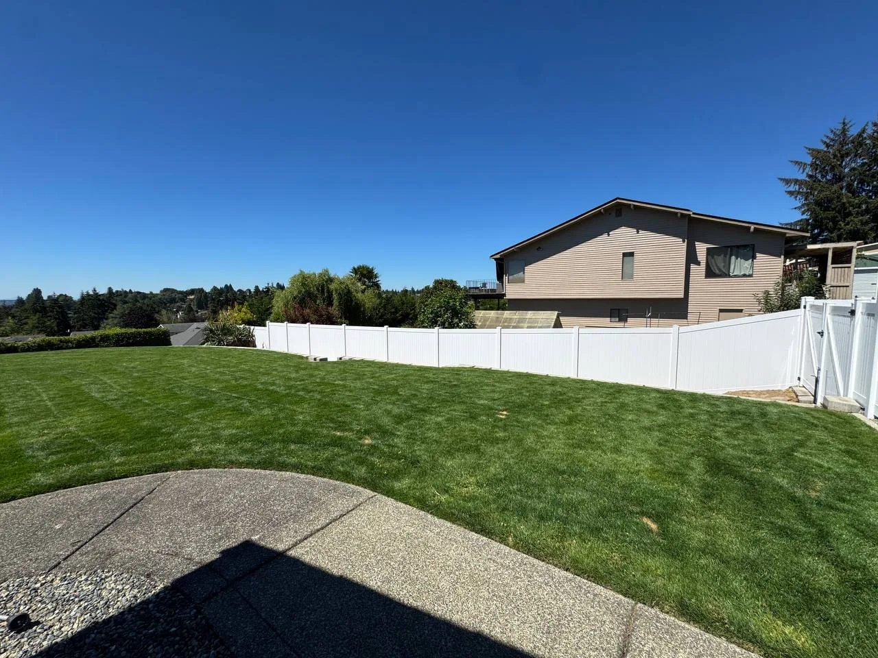 White vinyl privacy fence installed along a spacious backyard with green lawn, curved concrete patio, and white gate at a Bellevue residential property