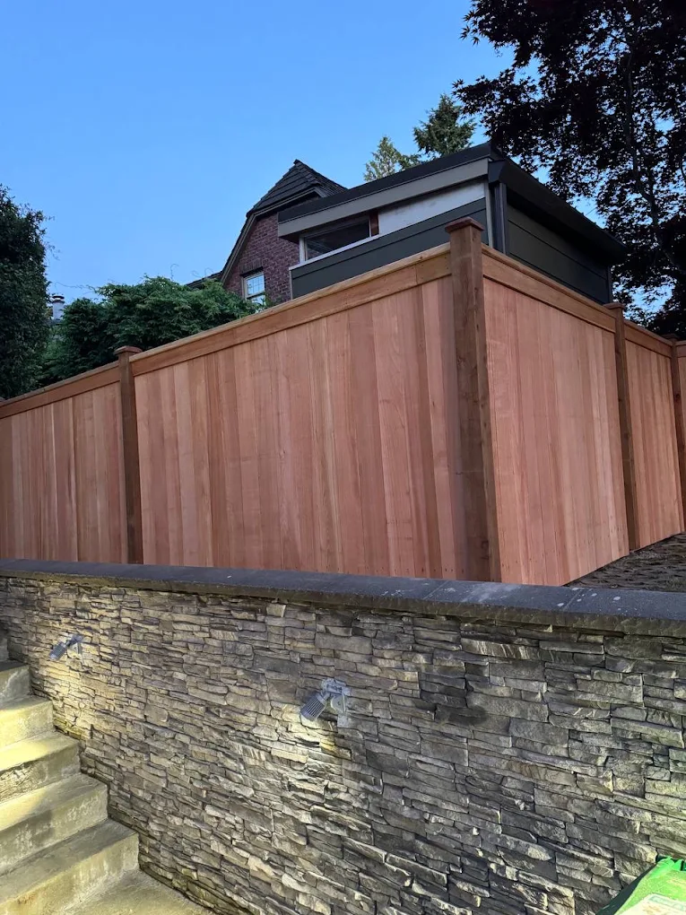 Cedar-toned faux wood vinyl fence with vertical board design and wood grain texture bordering a residential front yard with vibrant autumn red and pink foliage in Bellevue
