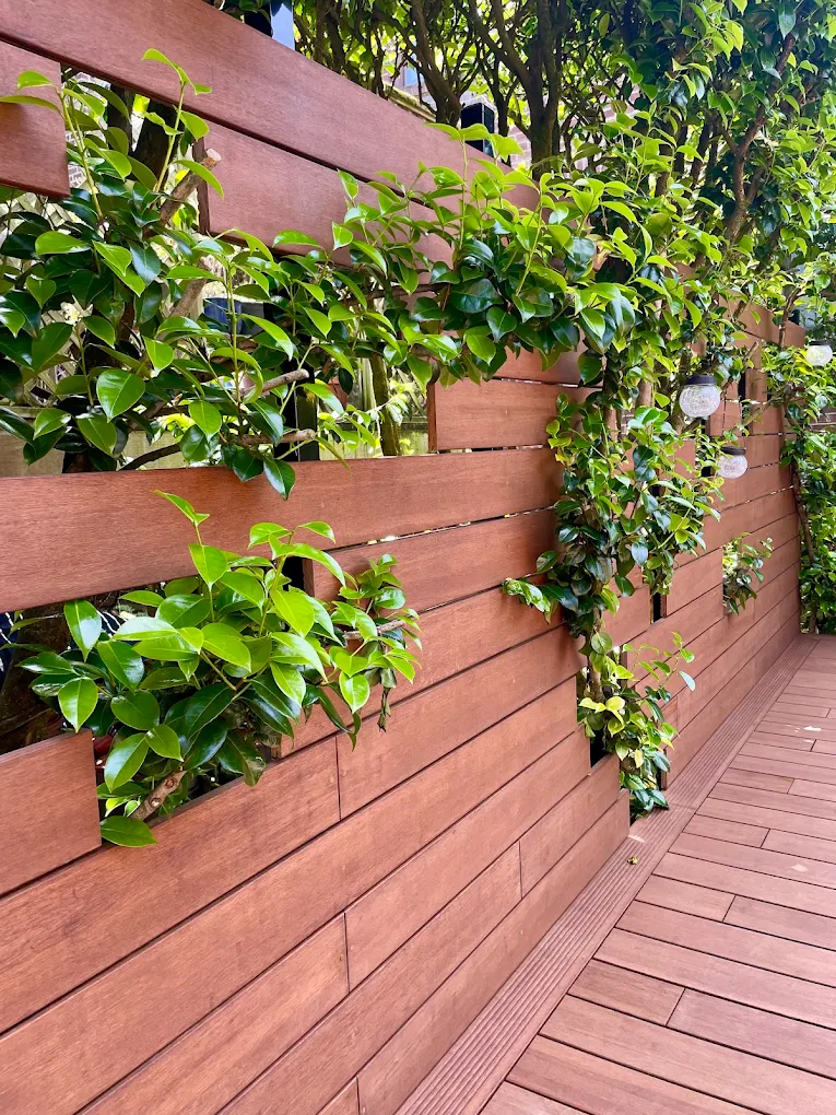 Brown faux wood vinyl fence with natural wood grain finish in a residential backyard with pink flowering vines and mature landscaping in Bellevue