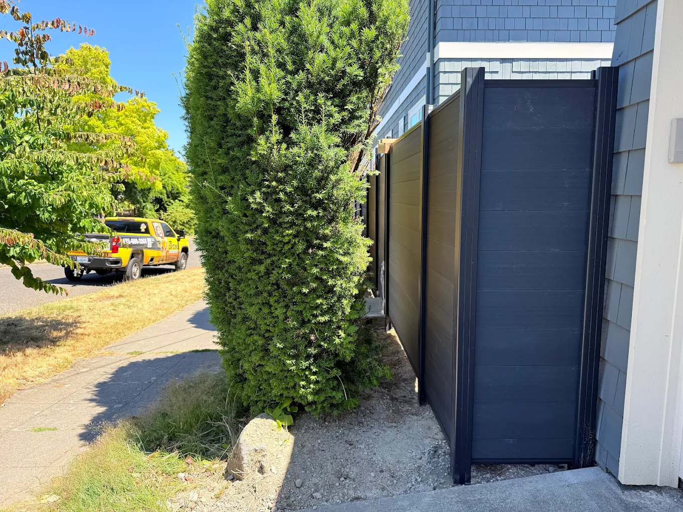 Dark charcoal horizontal vinyl fence with matching gate installed in a residential side yard with trimmed hedges and modern landscaping in Bellevue