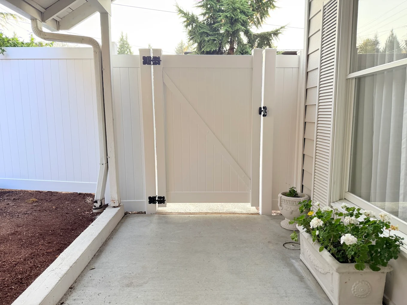White vinyl privacy fence with matching walk-through gate along a residential side yard professionally installed by Optima Fence and Deck