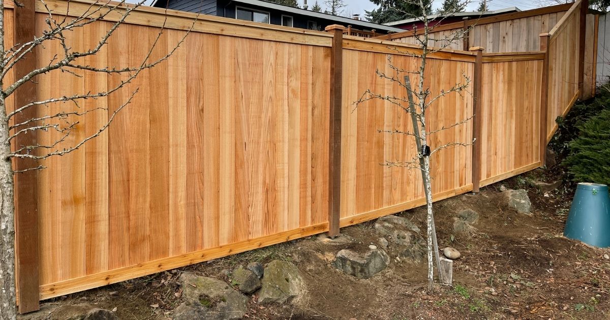 Cedar post on pipe fence installed on a sloped yard, featuring vertical cedar panels and elevated cedar posts