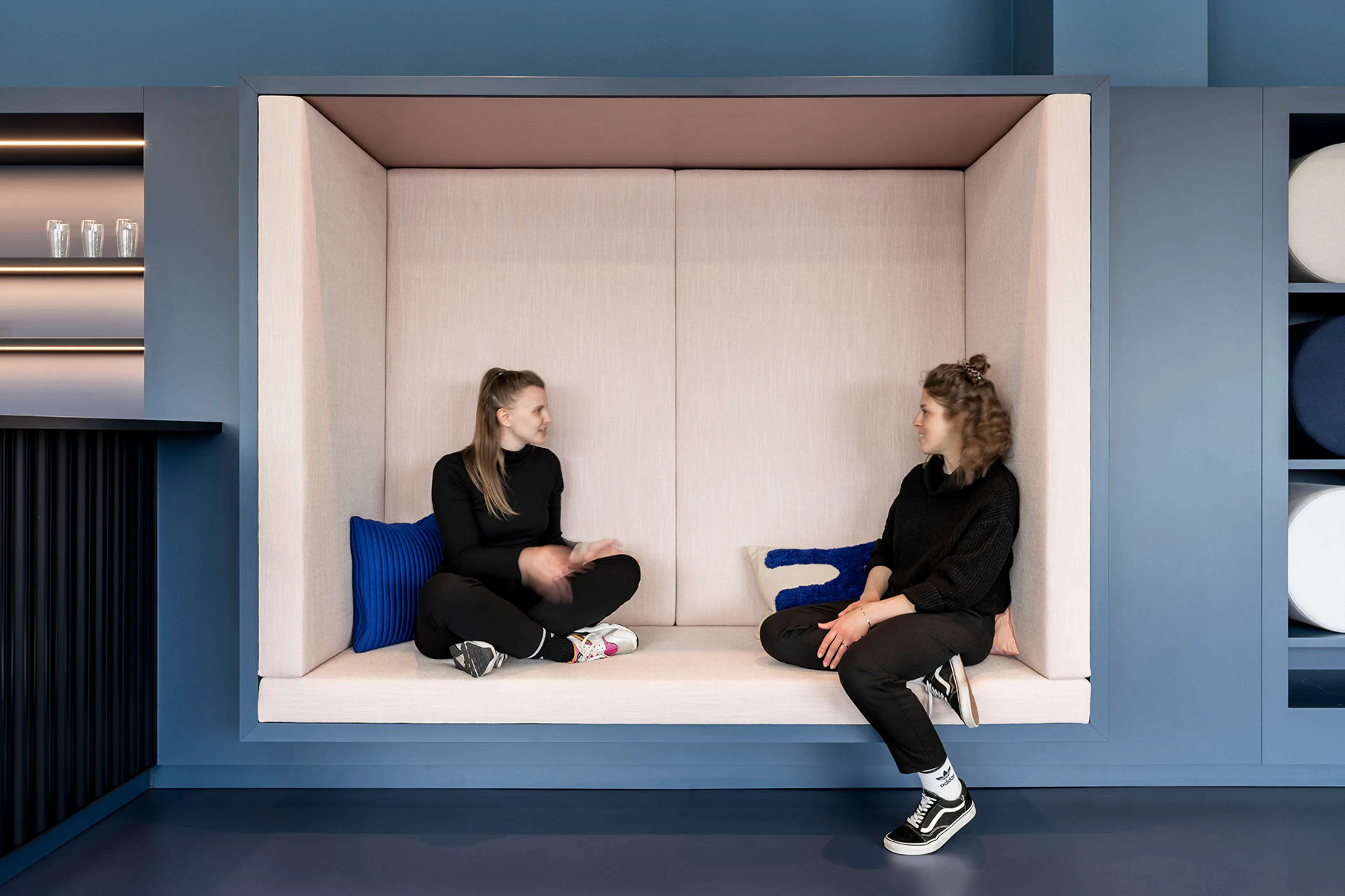 Zwei Frauen sitzen in einer modernen blauen Nische mit Kissen, die sich gegenüber sitzen und unterhalten.