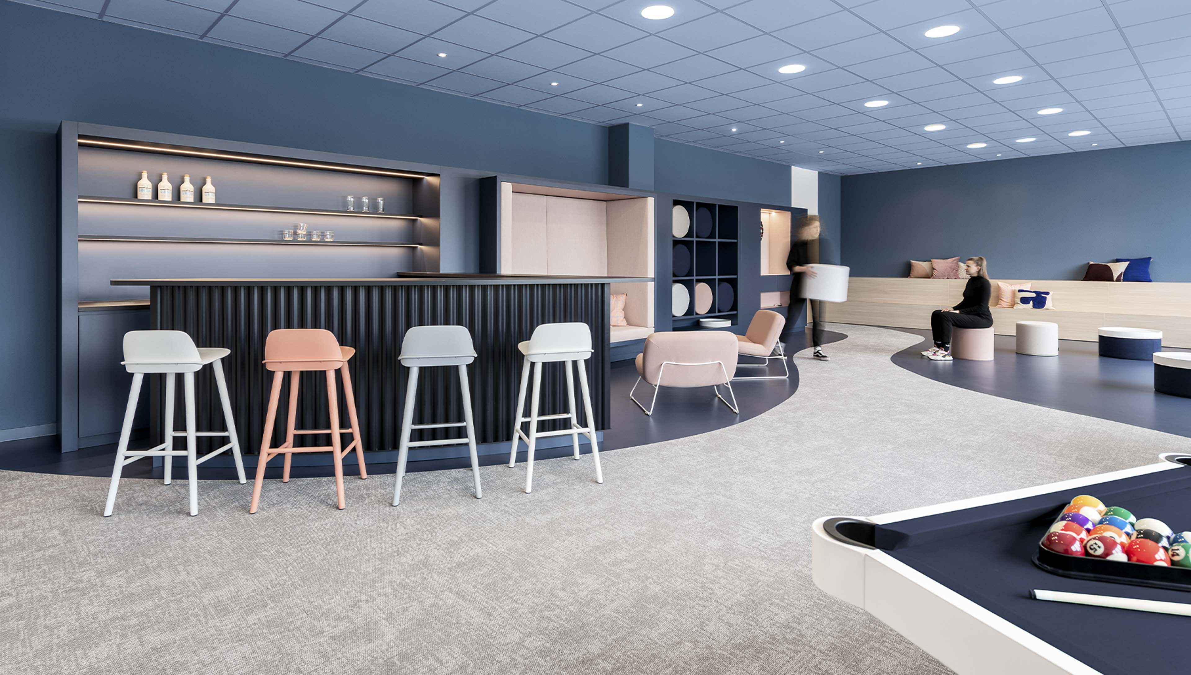 Moderner Aufenthaltsraum mit Bartheke, Hockern, Sitzgelegenheiten, zwei Personen und einem Billardtisch.