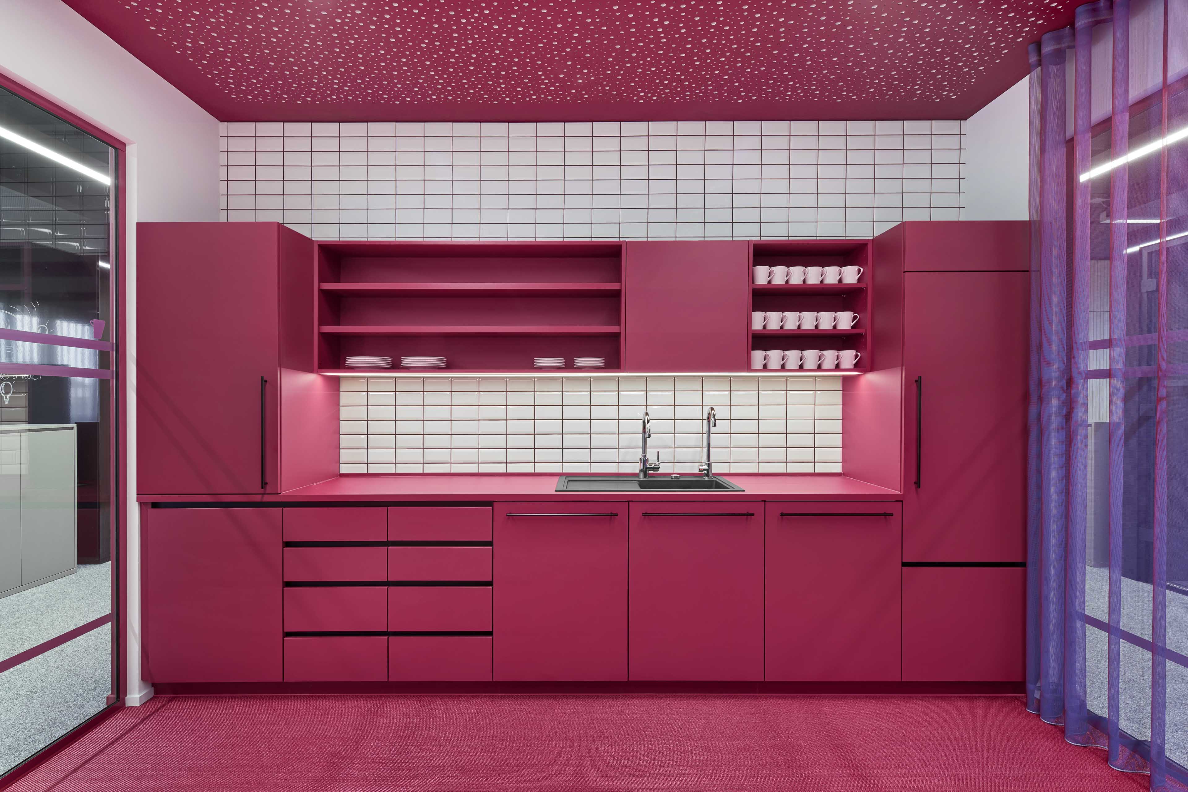 Moderne Küchenzeile mit pinkfarbenen Schränken, einem schwarzen Doppelspülbecken und weißen Tassen auf Regalen vor einer weißen Kachelwand.