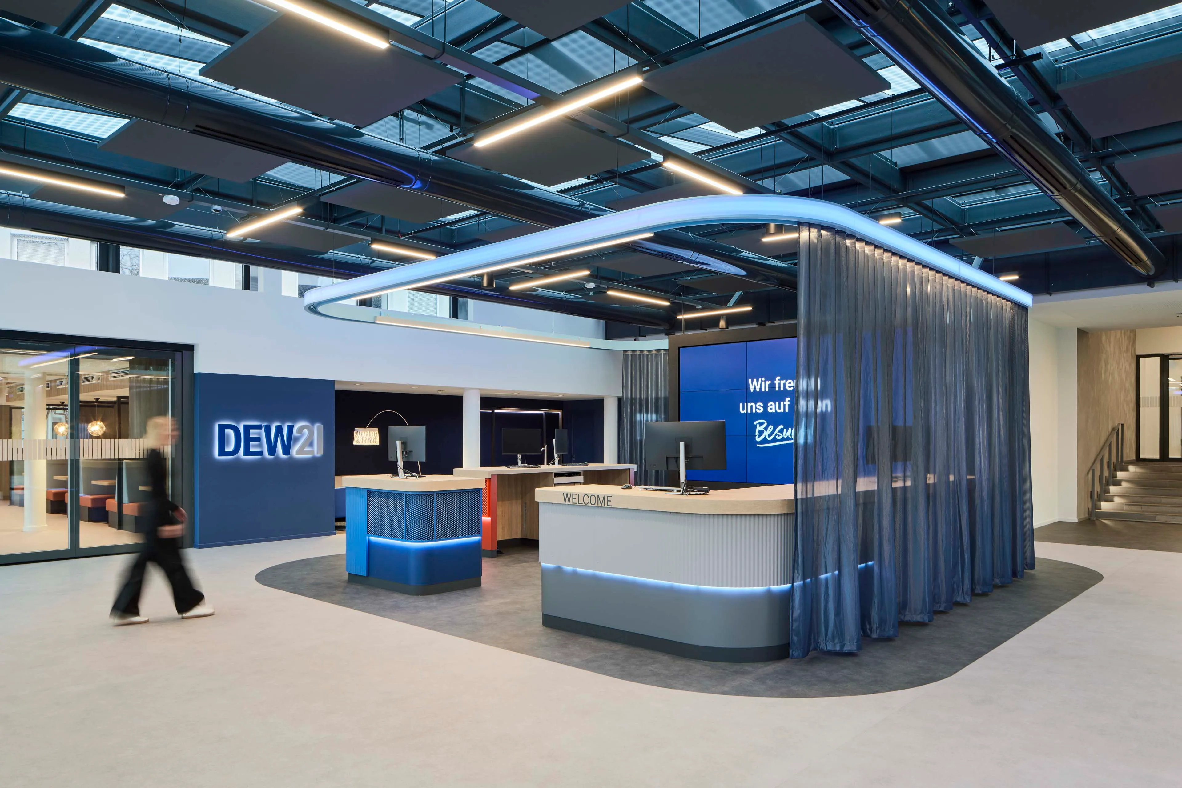 Modernes Empfangsbereich mit blau beleuchtetem DEW21-Schild, Schreibtischen mit Computern und blauen Vorhängen.