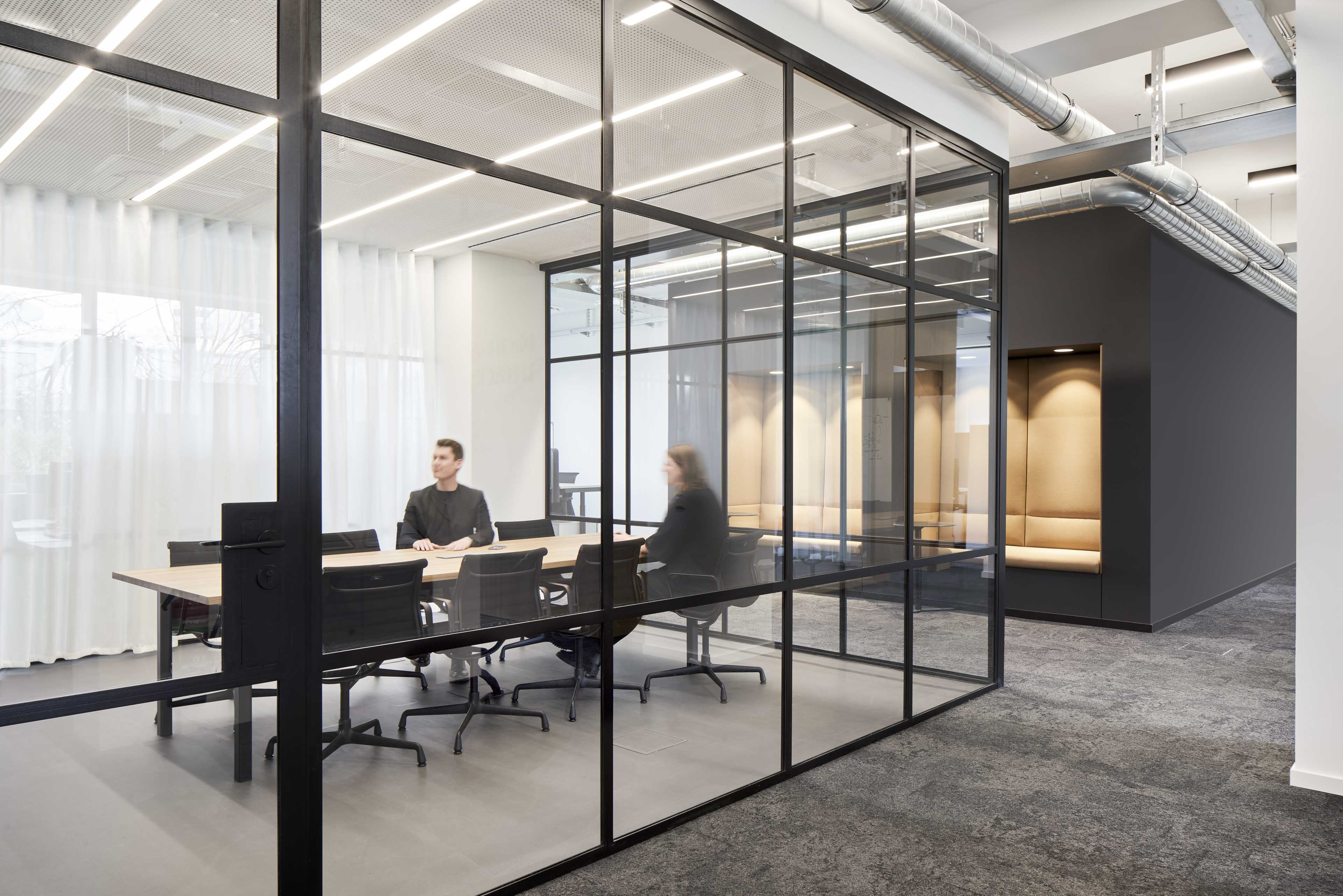 Modernes Büro mit Glastrennwänden, darin sitzen zwei Personen an einem Konferenztisch.