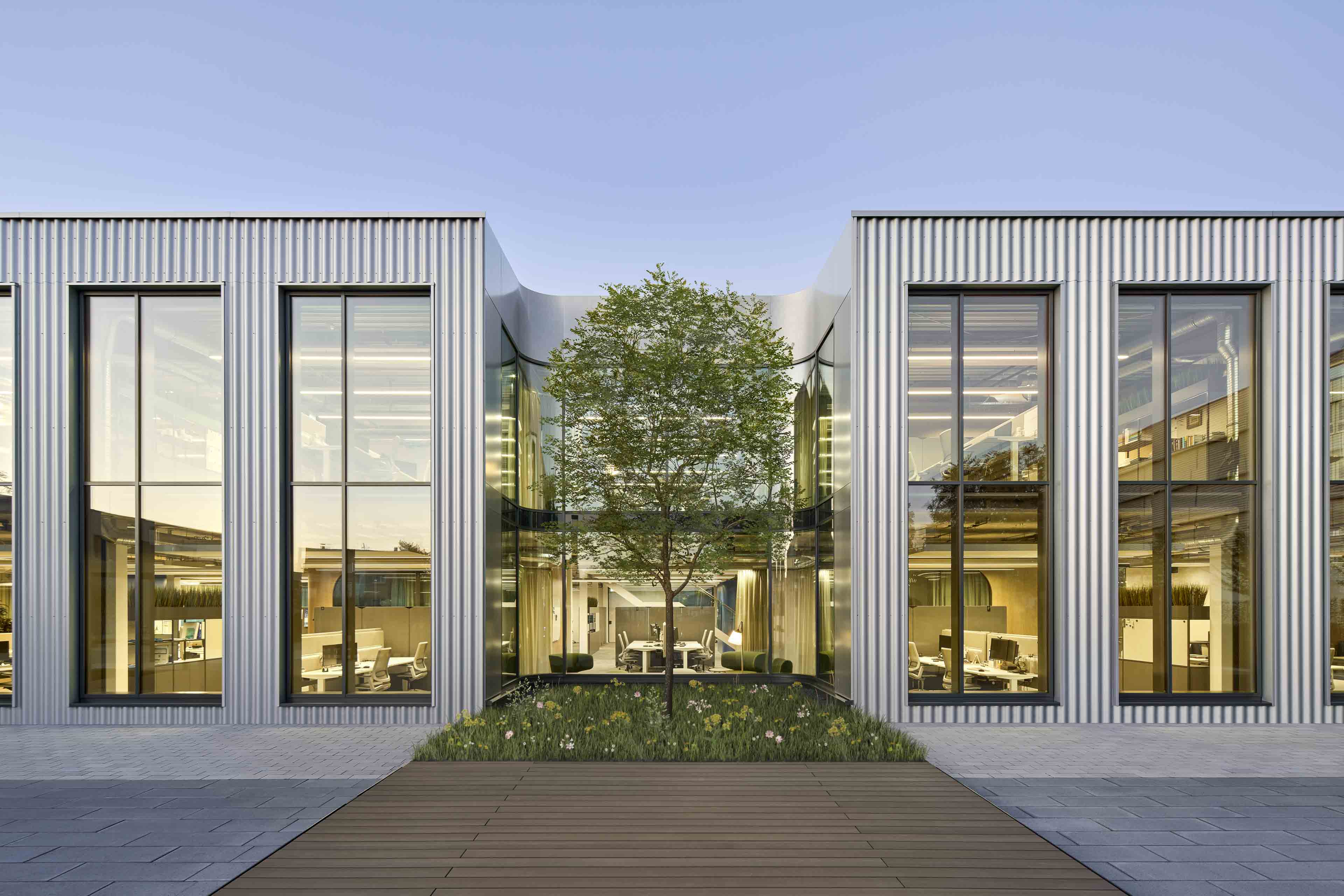 Moderne Bürogebäudefassade mit großen Glasfenstern und einem Baum in einem begrünten Innenhof.