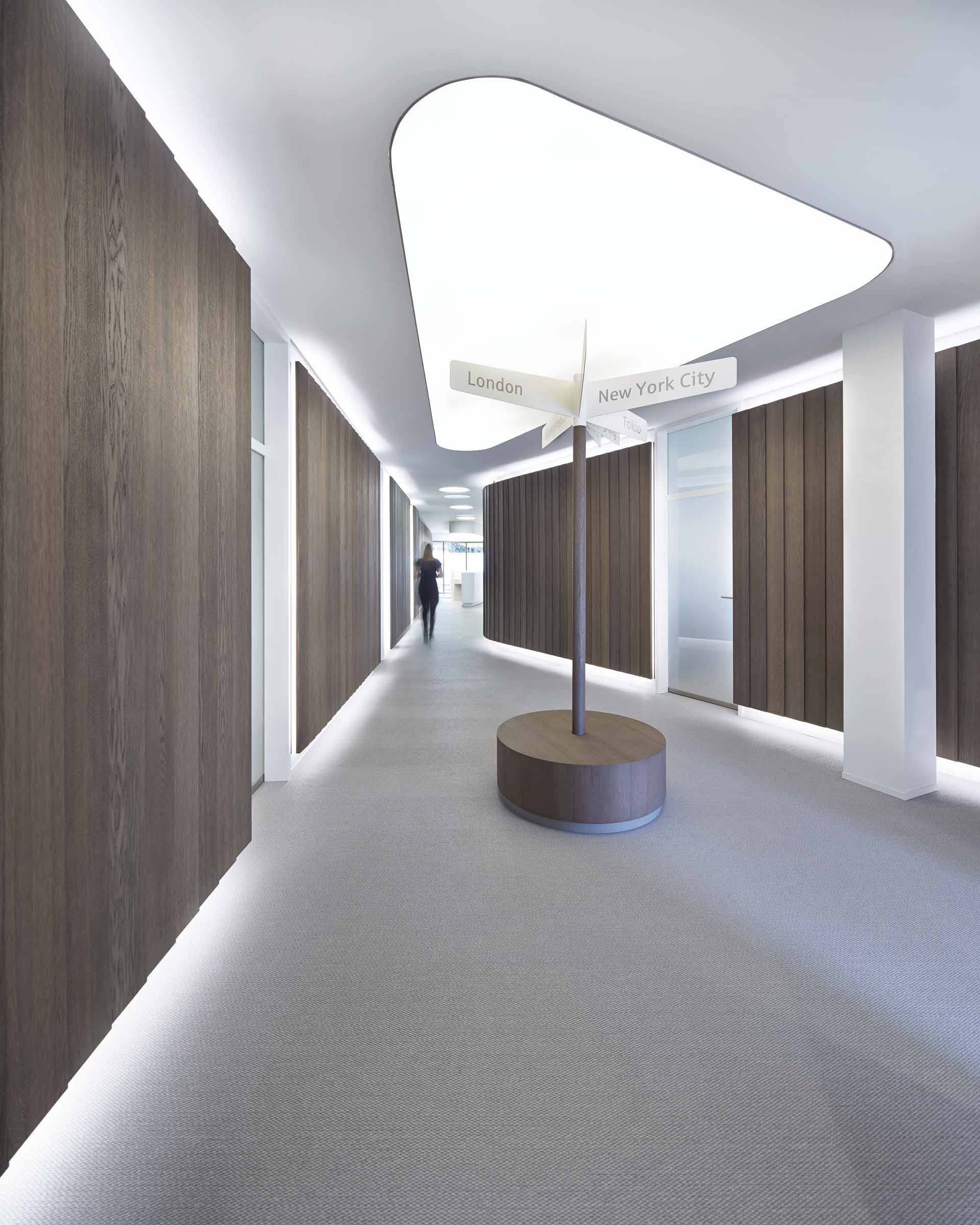 Moderner Flur mit Holzpaneelen, indirekter Beleuchtung und einem Wegweiser mit Richtungen nach London, New York City und Tokio.