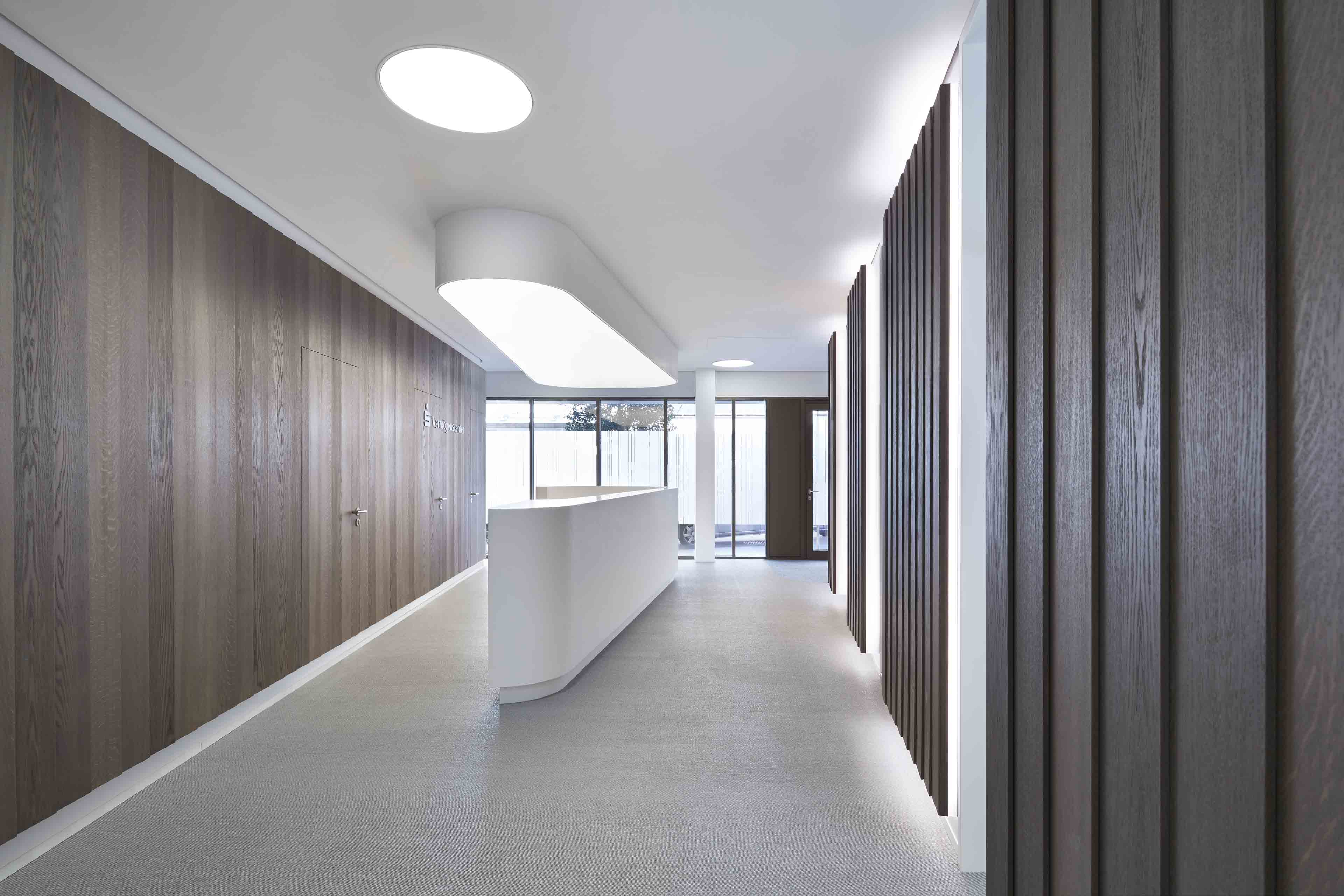 Moderner Empfangsbereich mit weißem Empfangstresen, Holzpaneelen an den Wänden und indirekter Deckenbeleuchtung.