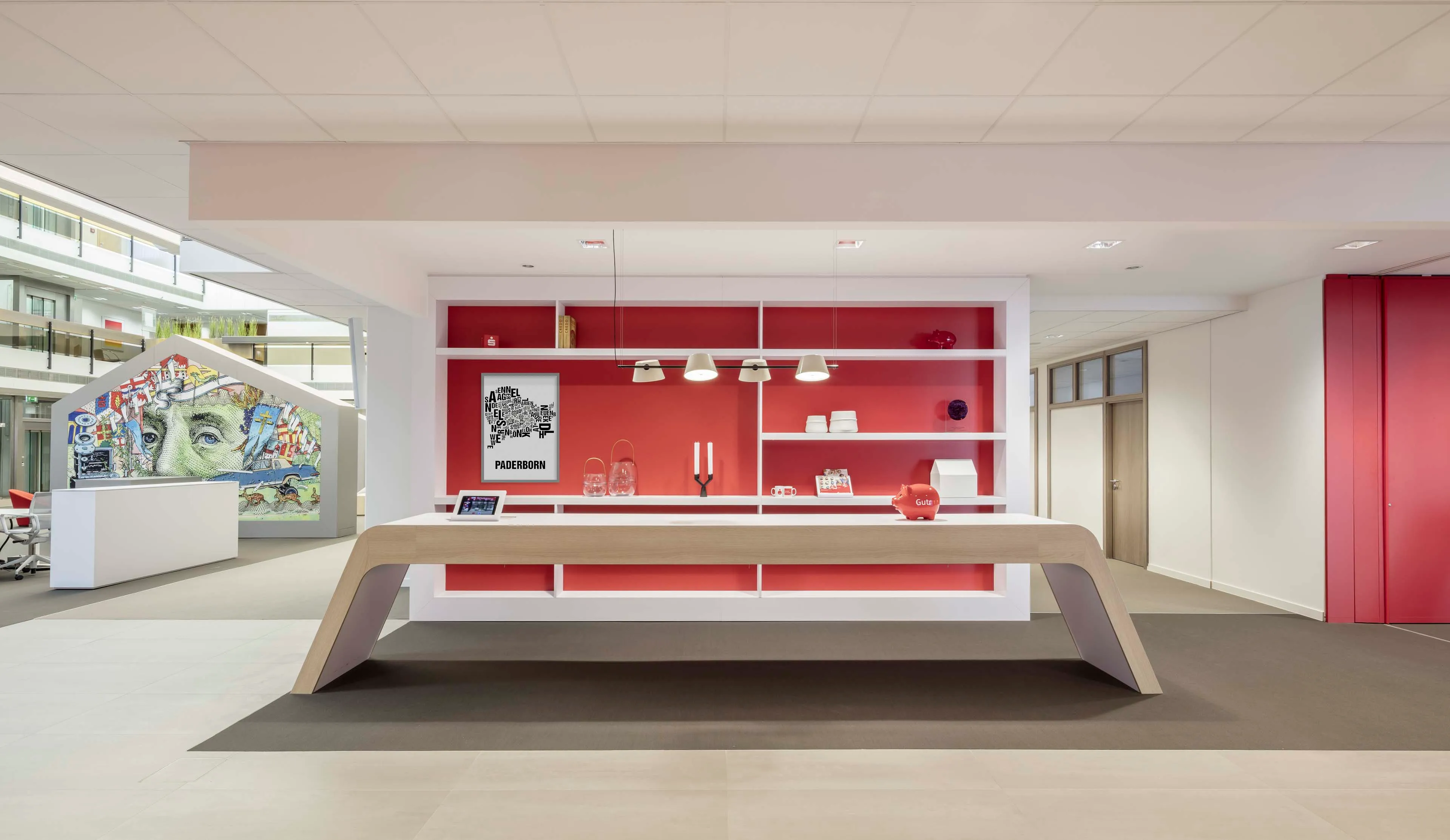 Moderner offener Innenraum mit einem großen Holztisch vor einem roten Wandregal und einer Wand mit künstlerischem Bild von Einstein.