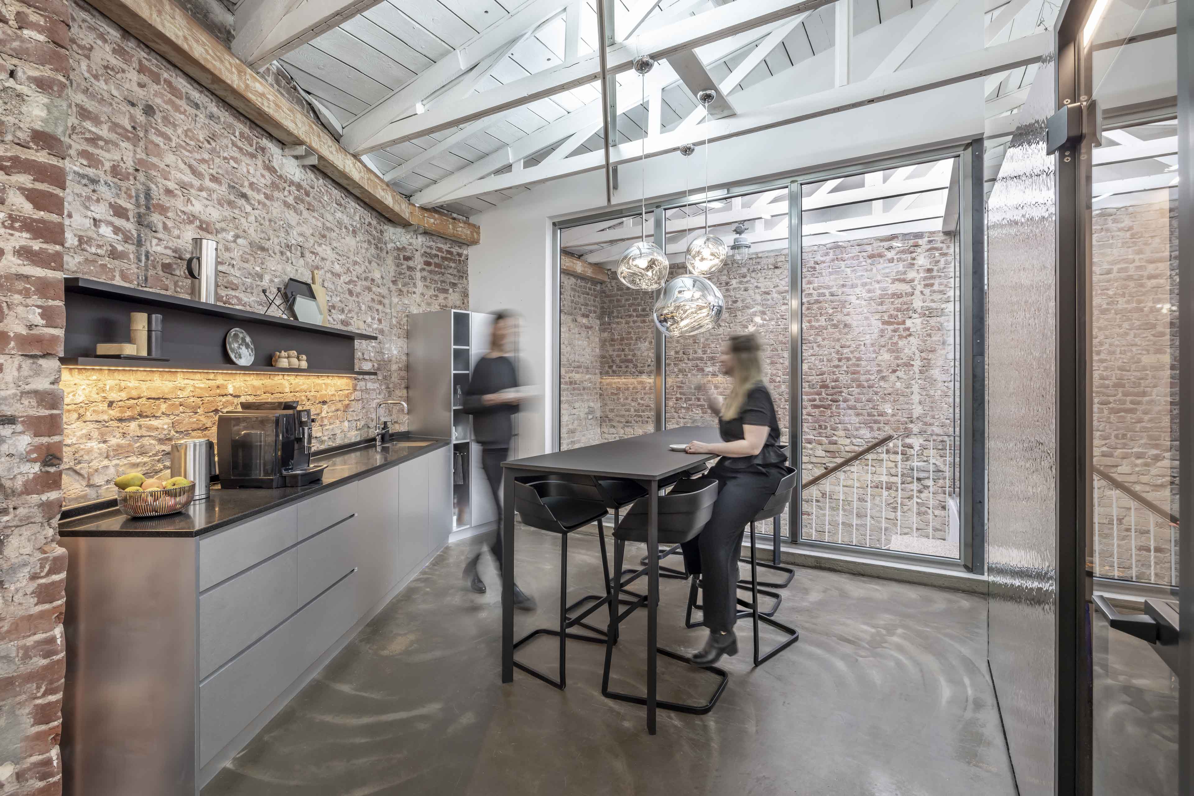 Modernes Büro mit freiliegenden Ziegelwänden, hoher Tafel und zwei Personen in Bewegung.