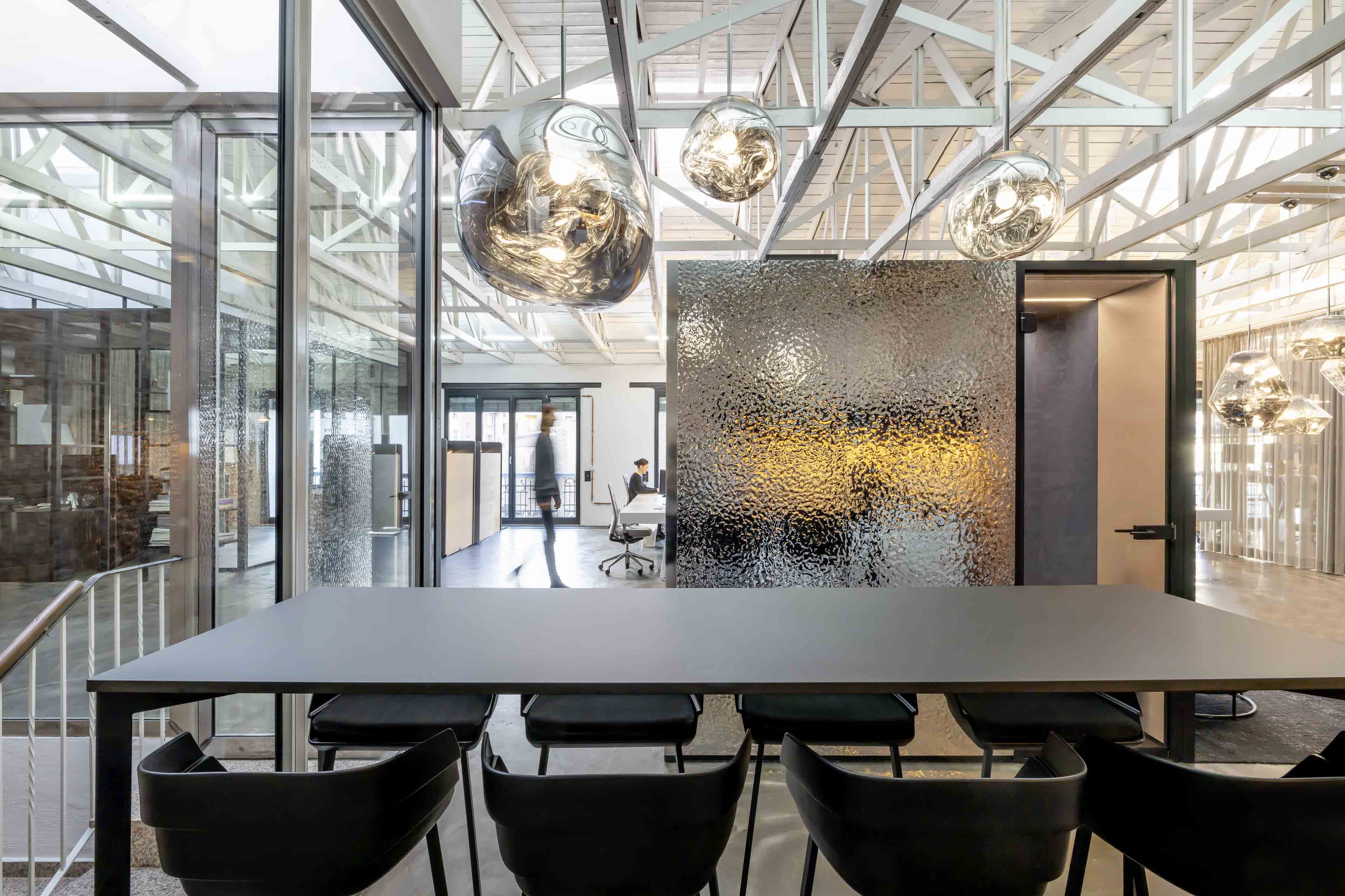 Moderner Büroraum mit schwarzem Tisch und Stühlen, gläsernen Trennwänden und hängenden Designerleuchten.
