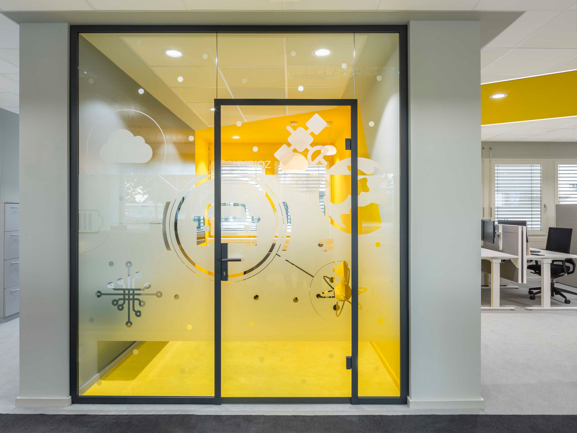 Modernes Büro mit Glaswand und Tür, die in einen gelb gestrichenen Besprechungsraum mit Symbolen für Technologie und Kommunikation führt.