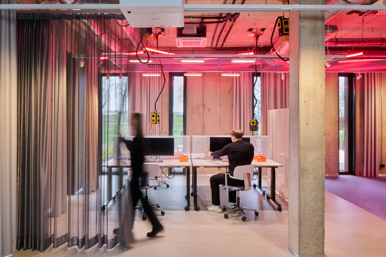 Ein moderner Büroraum mit vier Arbeitsplätzen, einem sitzenden Mann und einer Person, die vorbeigeht.