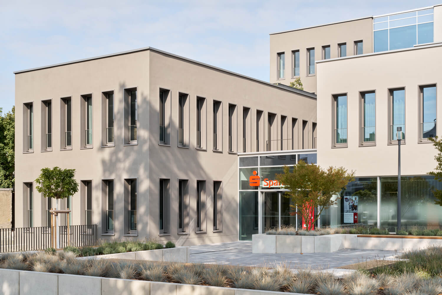 Modernes, helles Bankgebäude mit vielen schmalen Fenstern und einem Eingangsbereich mit dem roten Sparkassen-Symbol.