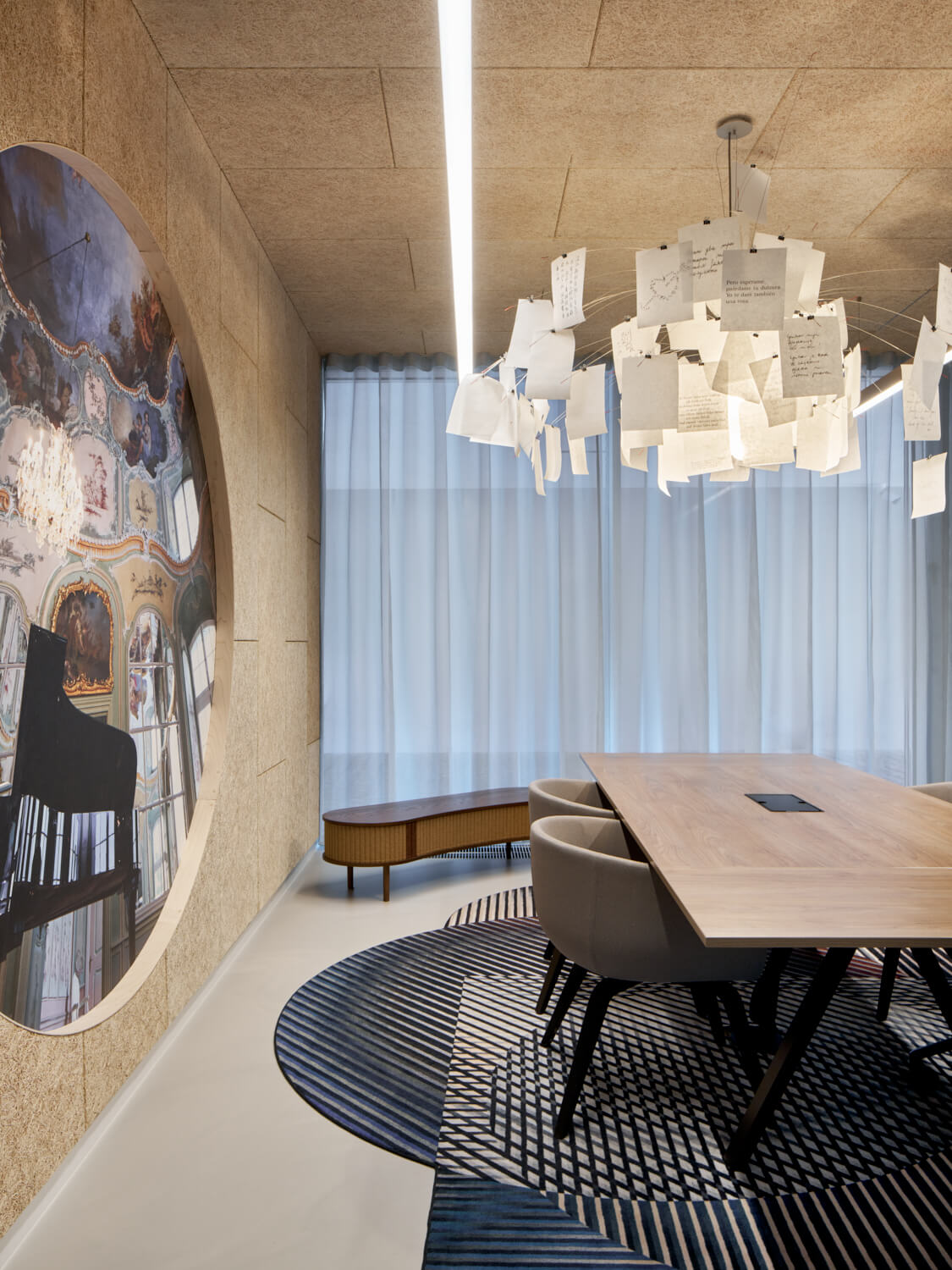Moderner Besprechungsraum mit einem Holztisch, hellgrauen Stühlen, rundem gemustertem Teppich und einzigartiger Deckenleuchte aus Papierblättern.