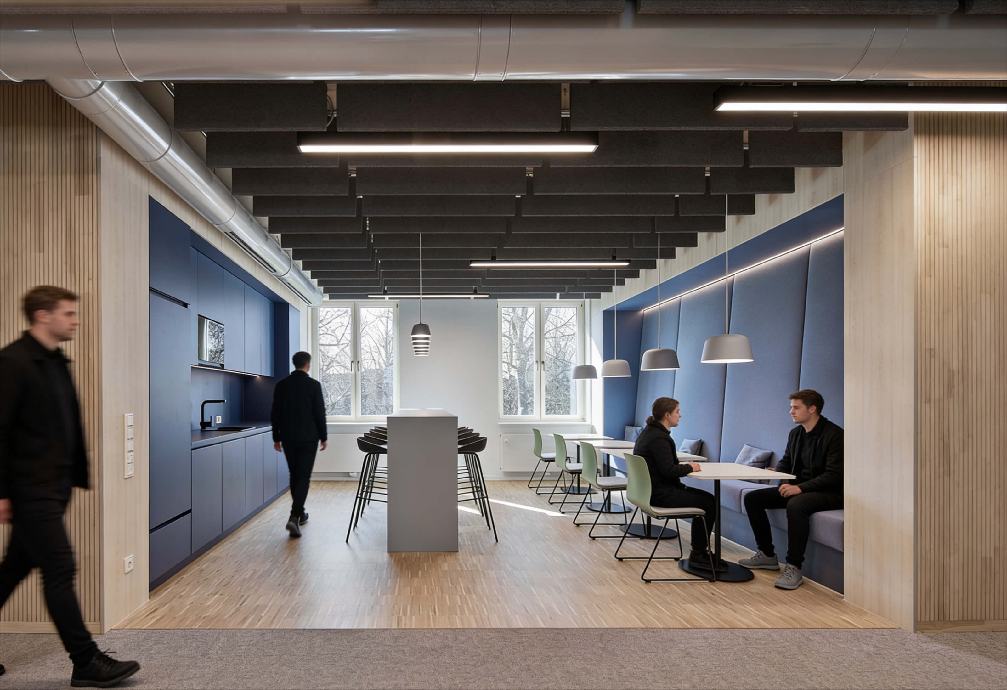Modern office kitchen and seating area with people sitting, walking, and standing around tables.