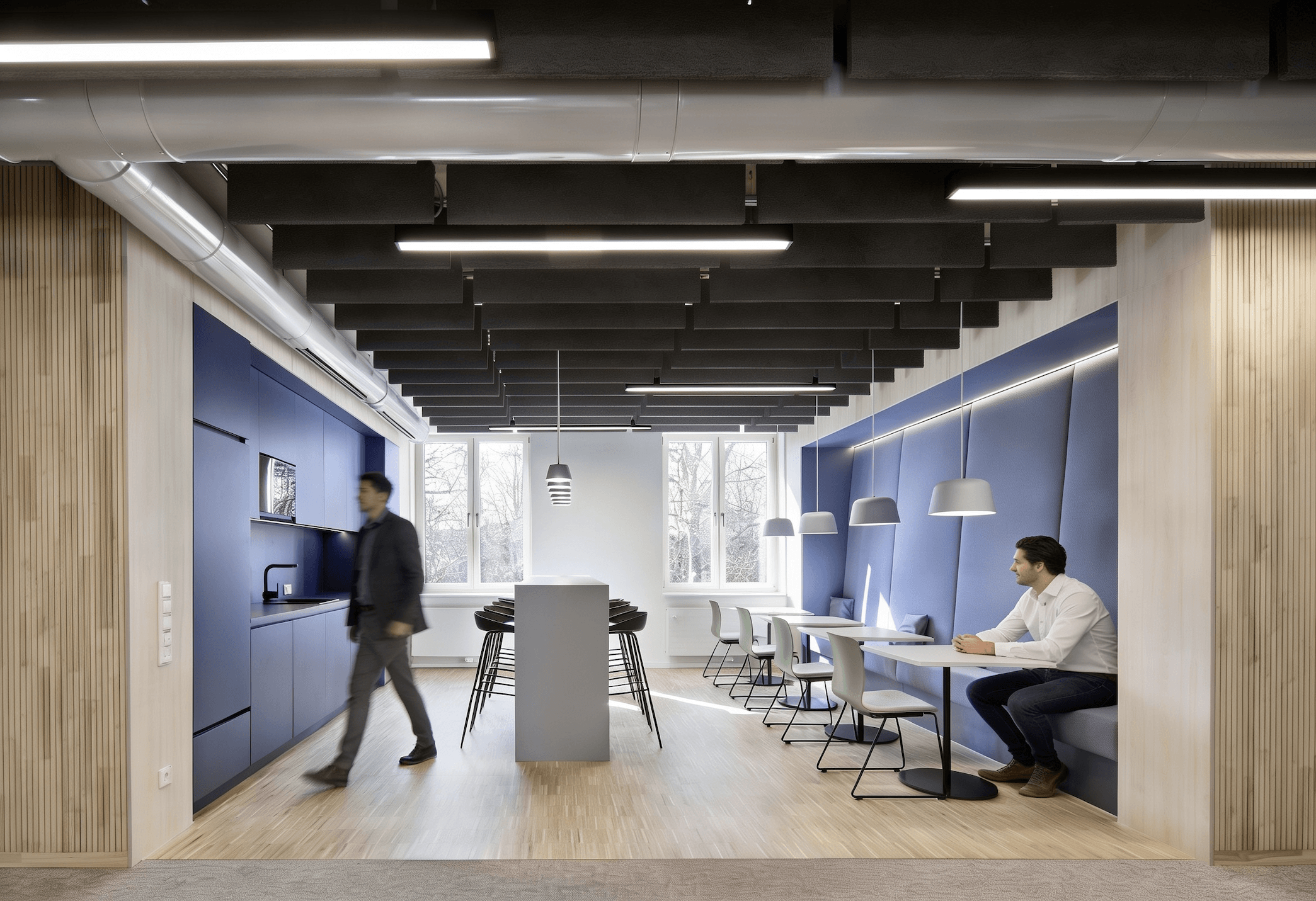 Moderner Pausenraum mit blauen Wandpaneelen, Tischen, Stühlen und zwei Männern in Businesskleidung.