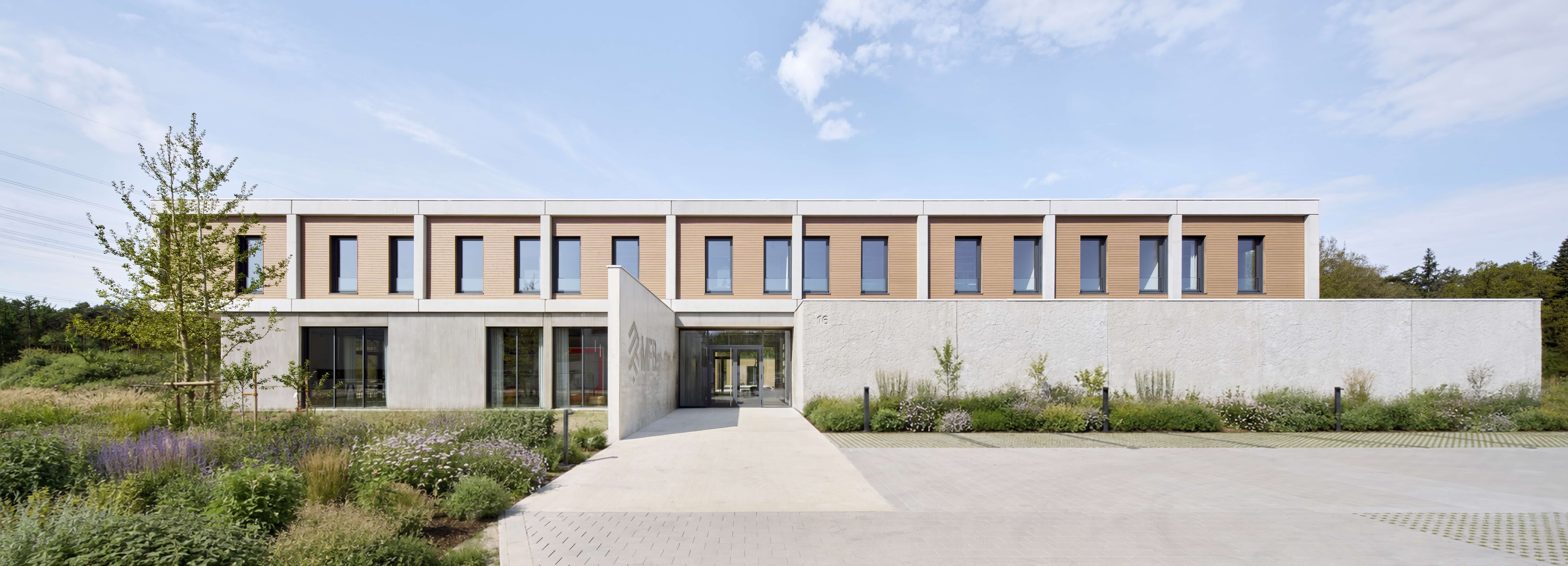 Modernes zweistöckiges Gebäude mit Holzfassade, großen Fenstern und umgeben von Pflanzen.