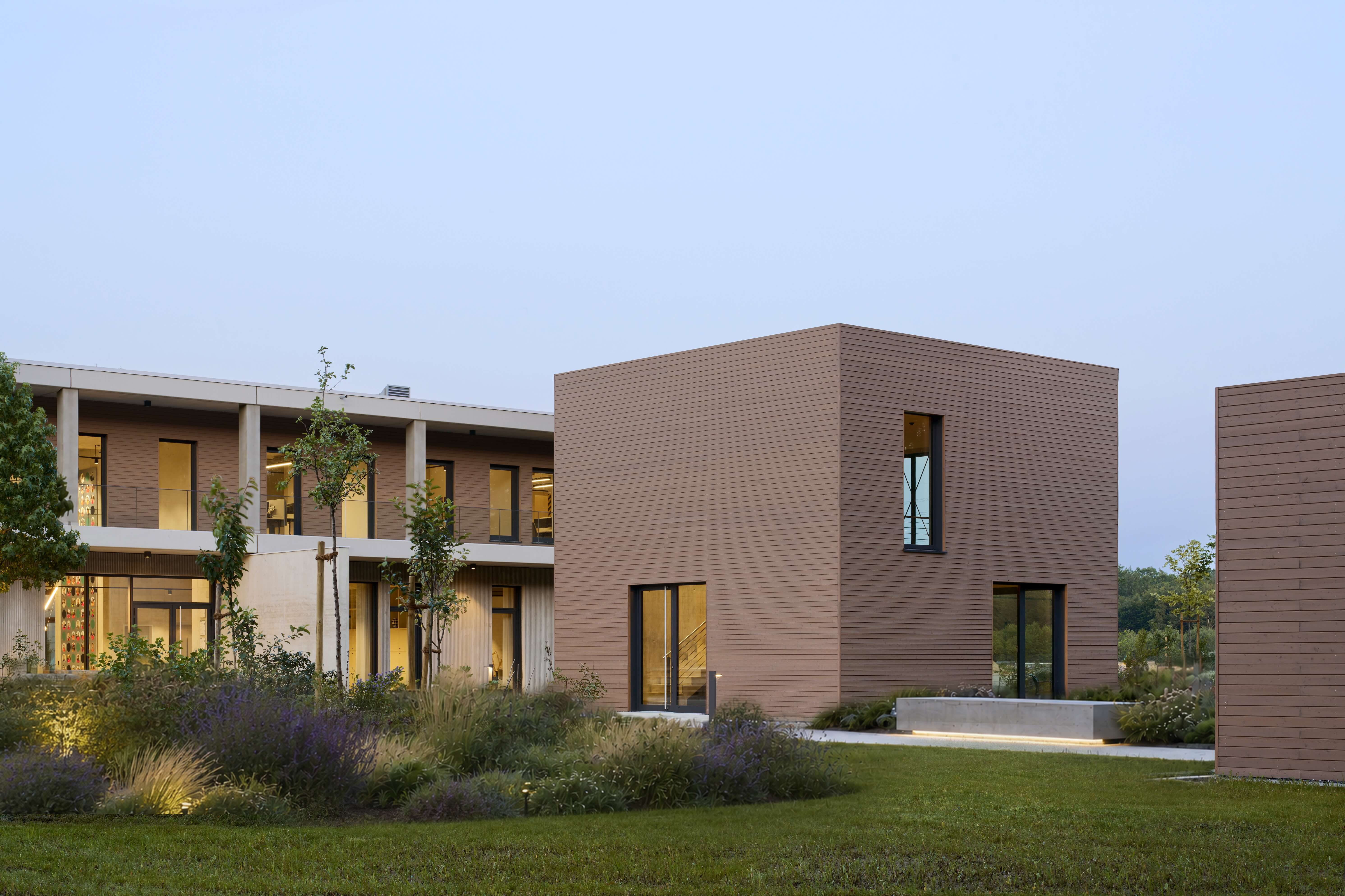 Modern zweistöckiges Gebäude und Tiny House mit großen Fenstern und Garten mit Büschen und Rasen.