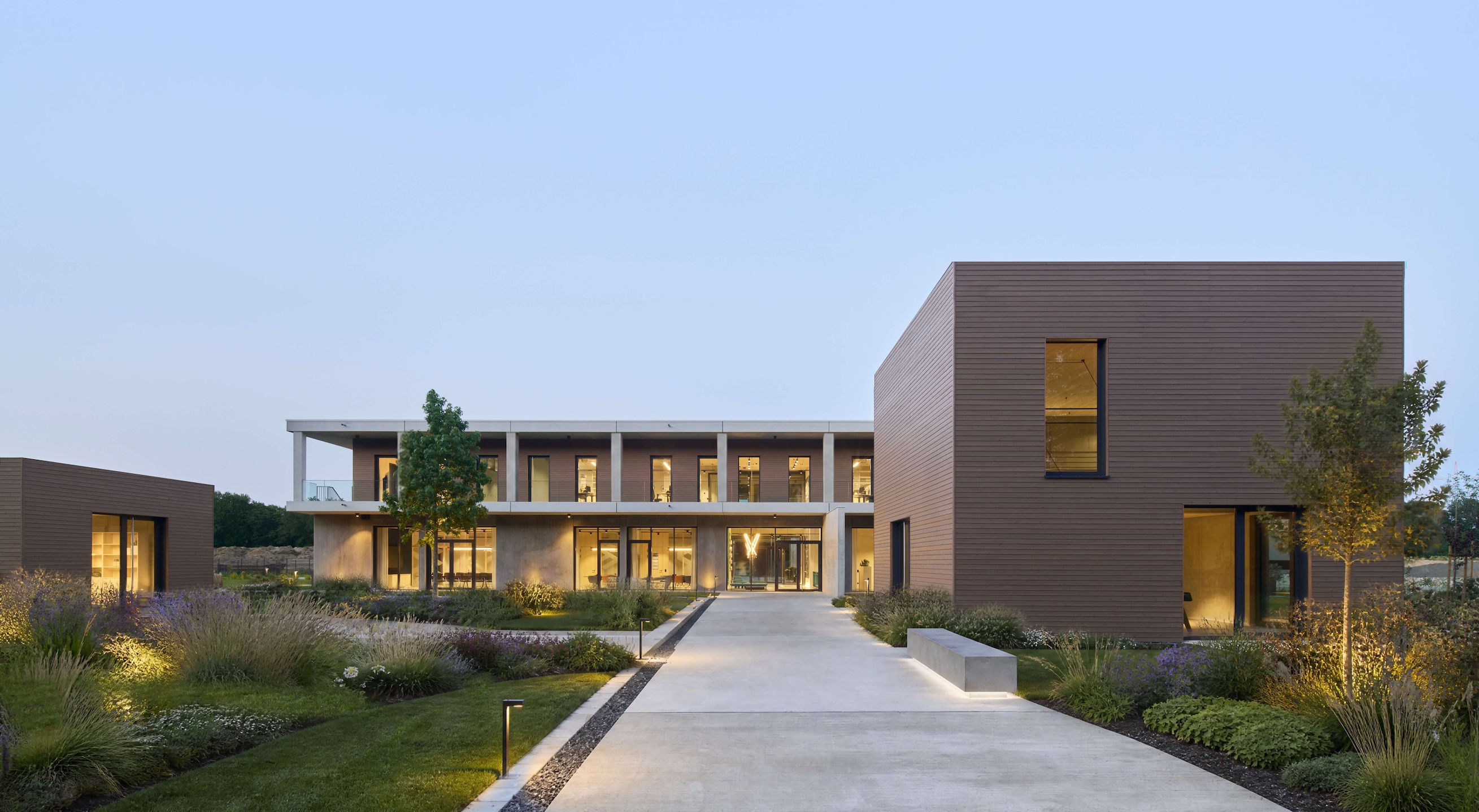 Modern office building with large windows, landscaped garden, and illuminated pathway at dusk.